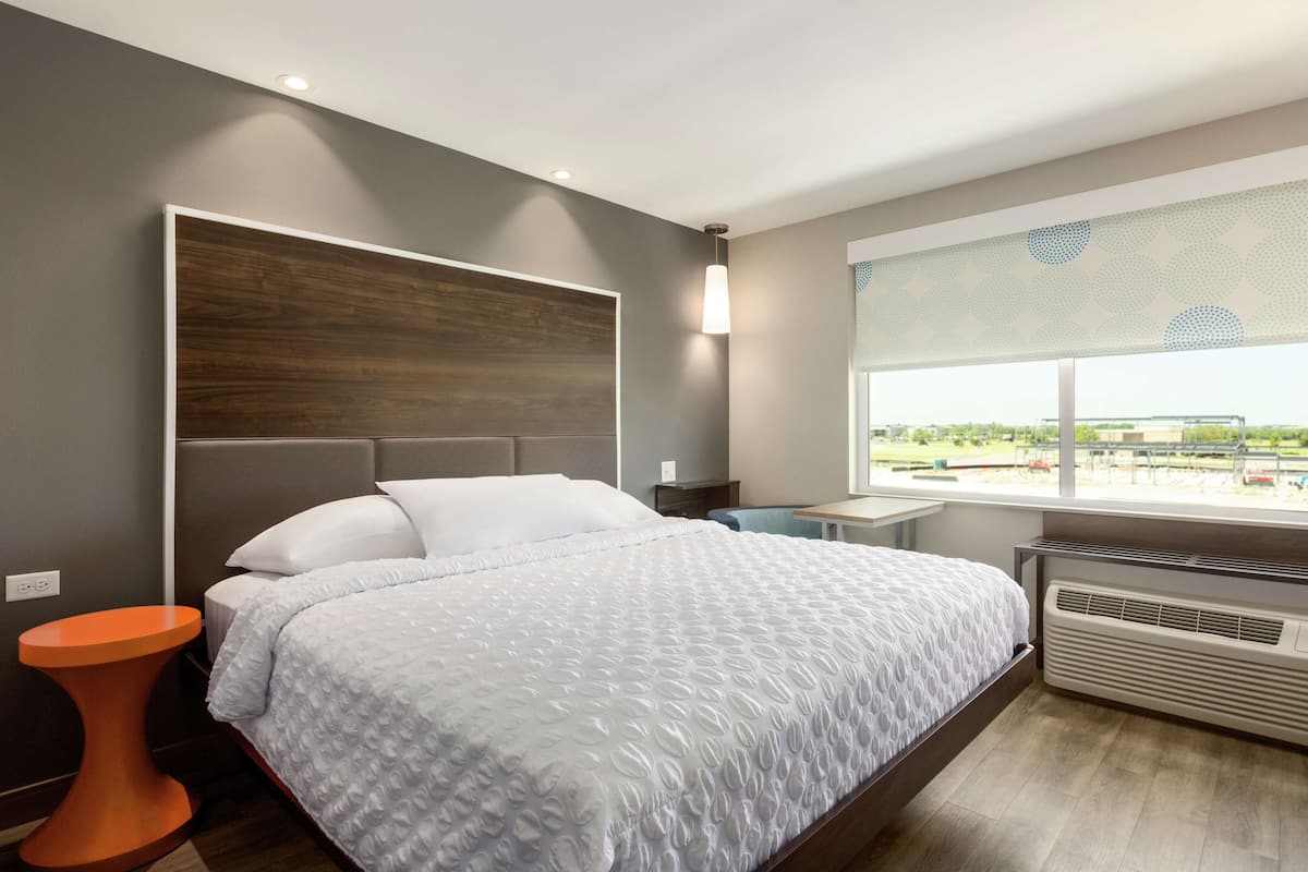 A modern bedroom with a large bed, a bedside table, a heater, and a window with a view.