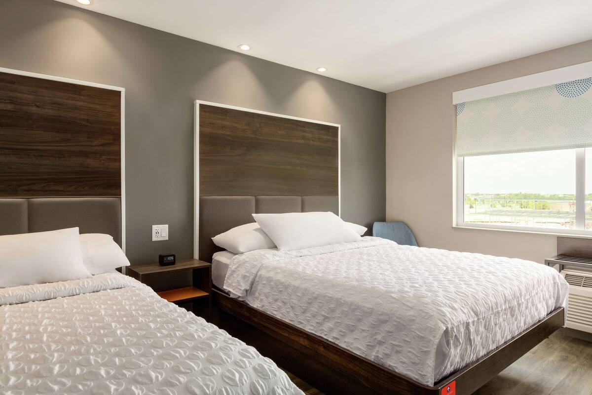 A modern hotel room with two beds, a large window with a view, and a built-in heater.