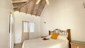 Un dormitorio con cama, mesita de noche, ventana con cortinas y ventilador de techo.