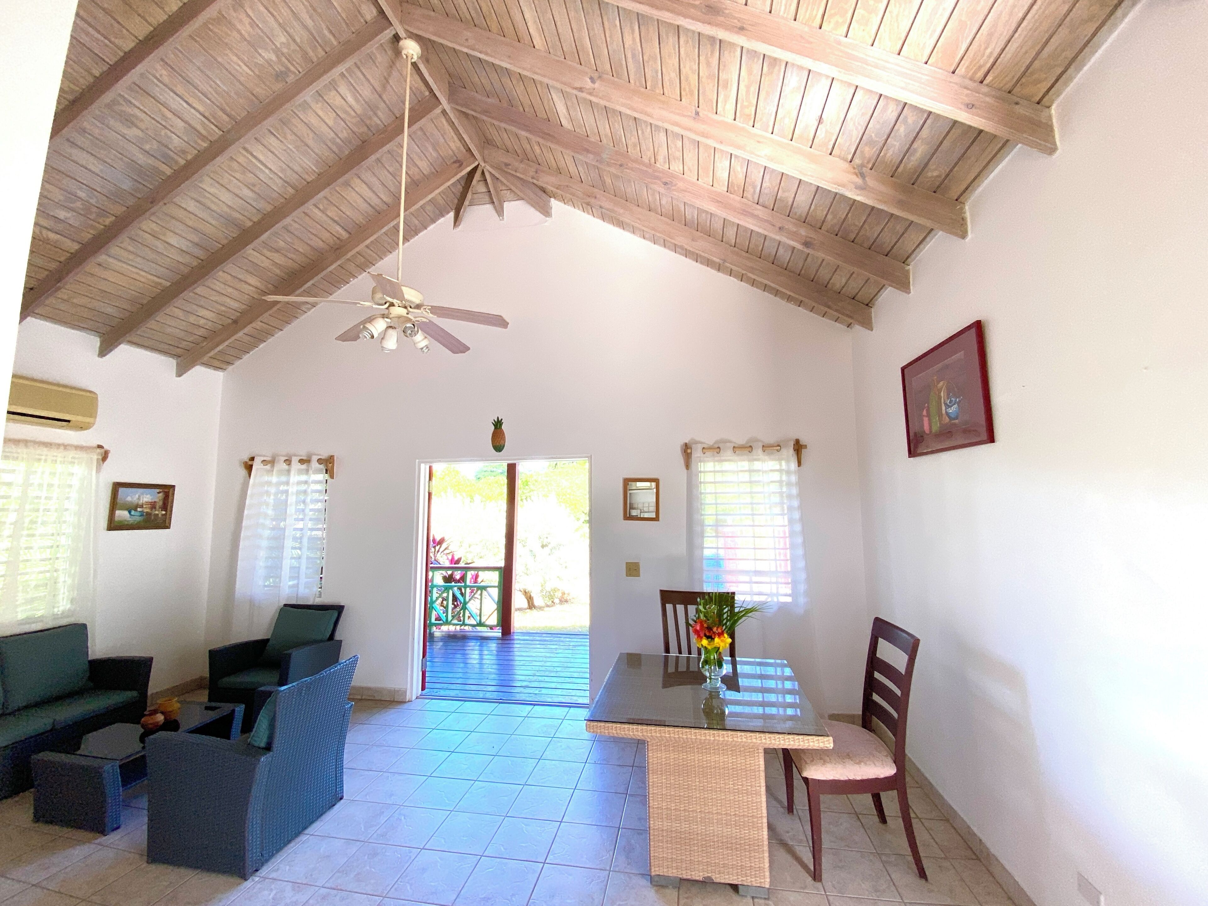 Un vaste espace de vie doté d’un haut plafond, d’un ventilateur de plafond, d’une table à manger avec des chaises et d’un ensemble de canapés.