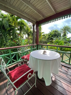 A covered outdoor seating area with a round table and metal chairs, surrounded by lush greenery. - The Greenside Cottages - Private Tropical Garden - Residential area 5 mins from the beach (St. John's)