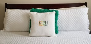 Een bed met witte gewatteerde beddengoed en een kussen met groene rand en een logo.