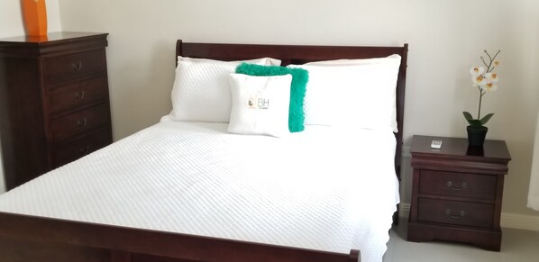 Een netjes opgemaakt bed met witte lakens en een groen sierkussen, met aan weerszijden donkerhouten nachtkastjes met lades.