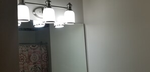Een badkamer met een spiegel, drie lampen en een badgordijn met een patroon.