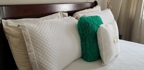 Een bed met een geborduurde witte matras, een houten hoofdbord en een groen, zacht kussen.