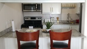 A kitchen with white cabinets, a stainless steel microwave, a black stove, and two wooden chairs at a granite countertop. - New Kingston Guest Apt at Kingsway (Kingston)