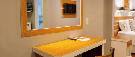 Una habitación pequeña y bien iluminada, con un escritorio de madera, una silla y un espejo grande sobre el escritorio.