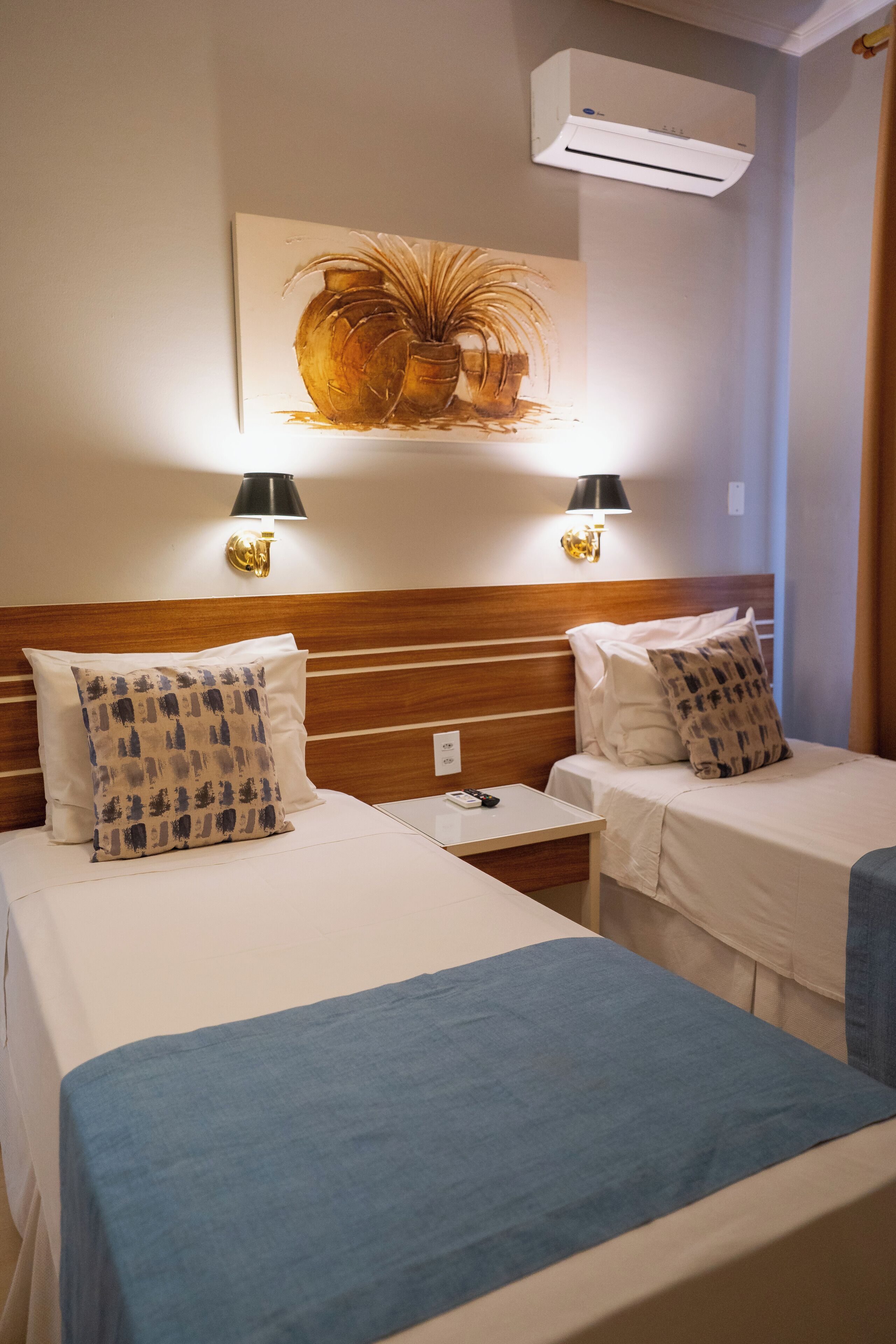 A hotel room with two beds, a wooden headboard, a wall-mounted air conditioner, and a painting above the beds.