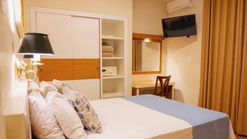 A hotel room with a bed, bedside table with a telephone, a desk with a chair, a television mounted on the wall, and a wardrobe.