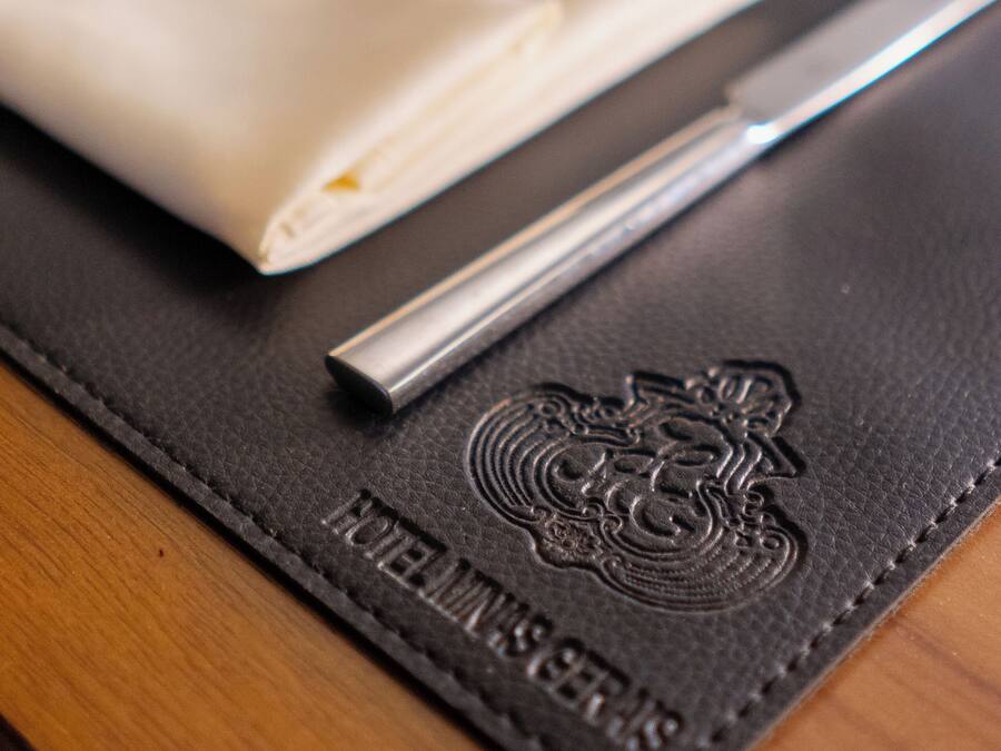 A table setting with a folded napkin, a knife, and a fork on a black leather placemat with embossed text.