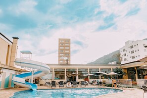 Un área de piscina con tobogán de agua, sillas de descanso y sombrillas.