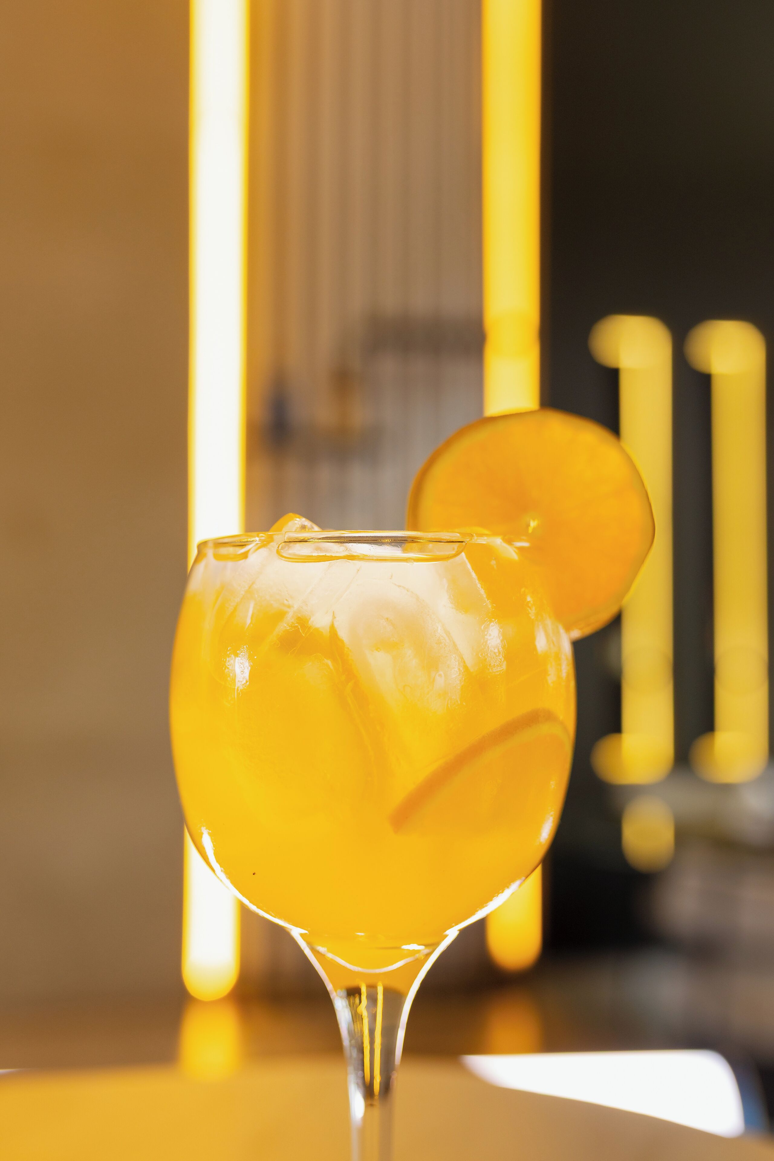 A cocktail glass with a clear liquid and a slice of fruit on the rim, placed on a reflective surface.