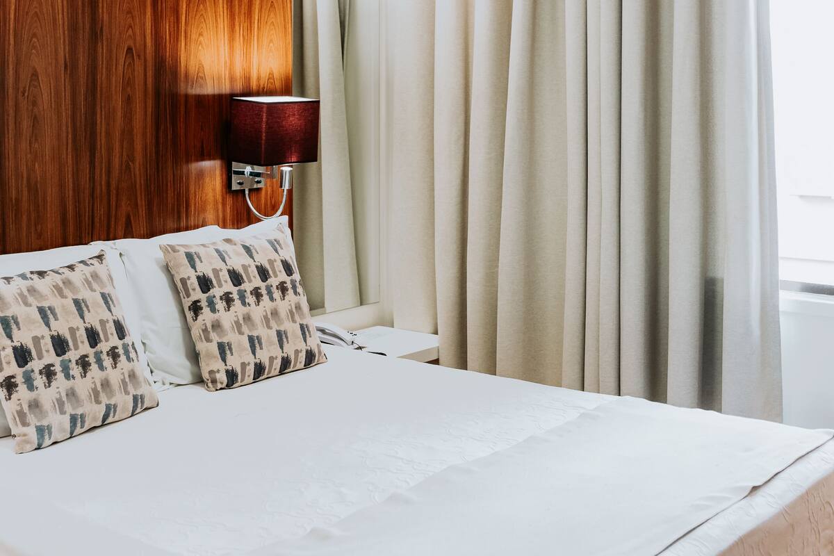 Ein Hotelzimmer mit einem großen Bett, beigen Vorhängen, einem Holzkopfschild und einer Wandlampe.