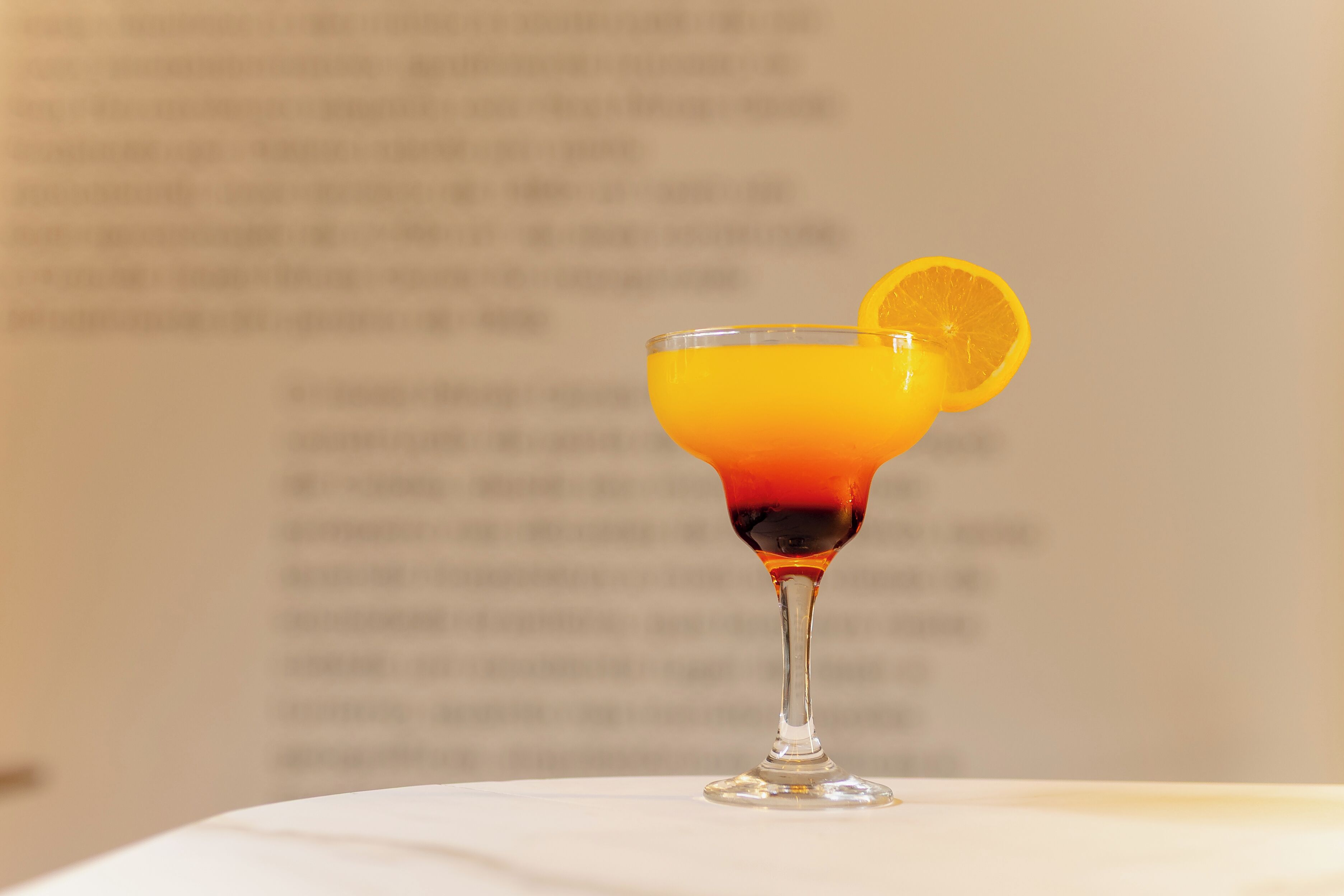 Ein Cocktailglas mit Farbverlauf, einer Orangenscheibe und unscharfem Hintergrund mit Text.