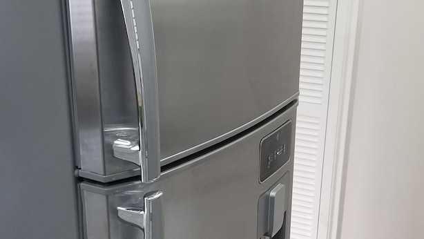 A stainless steel refrigerator with a water and ice dispenser, located in a room with white walls and a tiled floor.