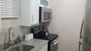 A compact kitchen with a sink, a toaster, a kettle, a microwave, and a refrigerator.