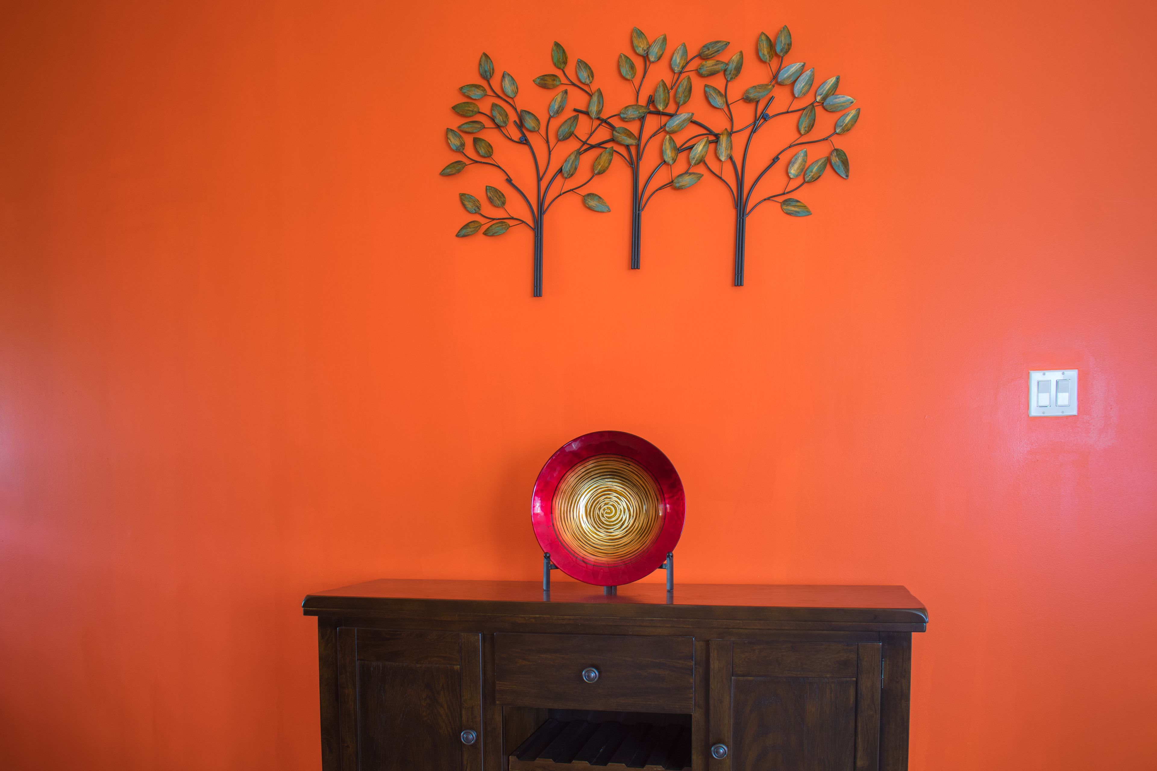 A wall with a red circular object on a wooden cabinet.
