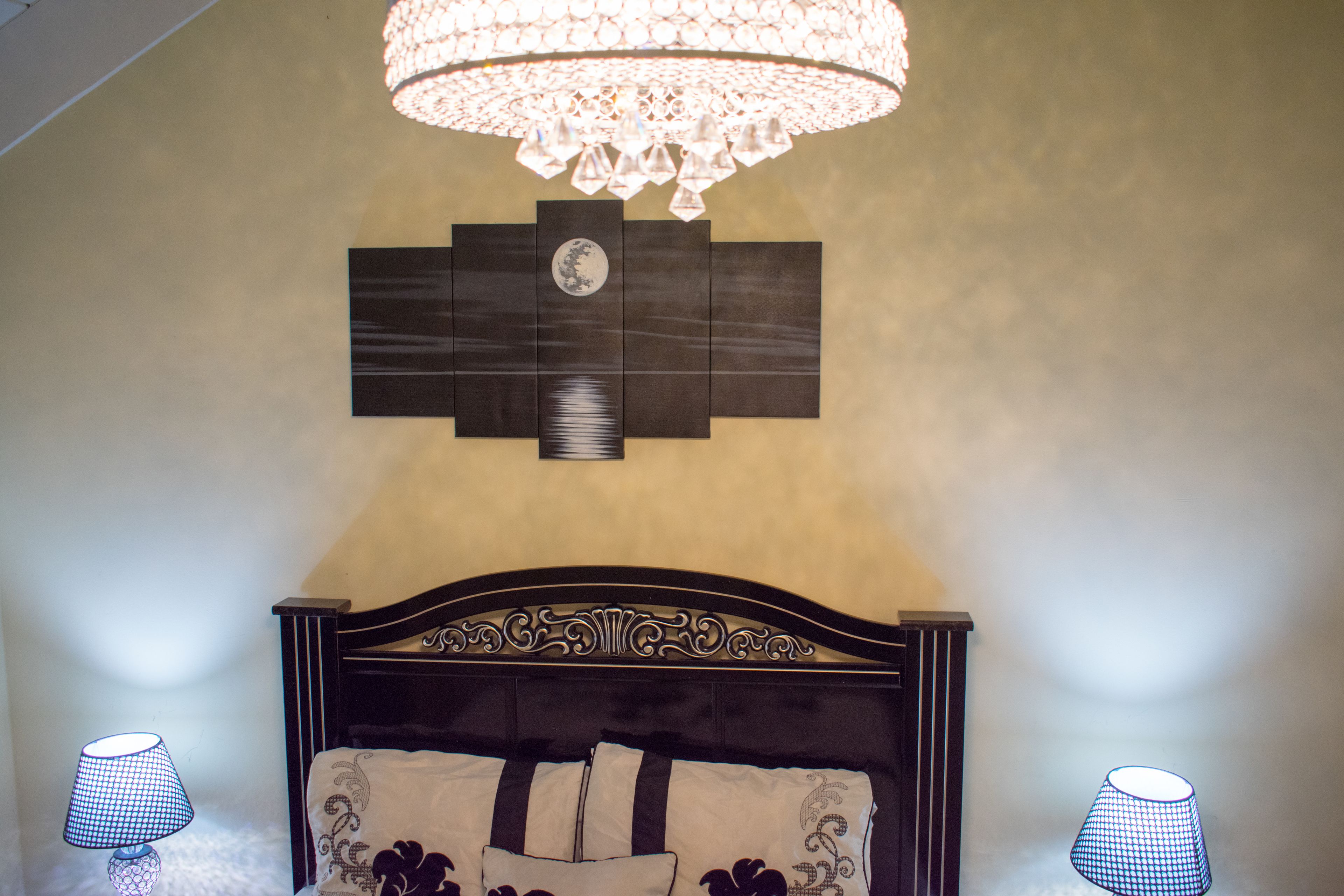A bedroom with a dark wooden headboard, a chandelier, and two lamps on either side of the bed.
