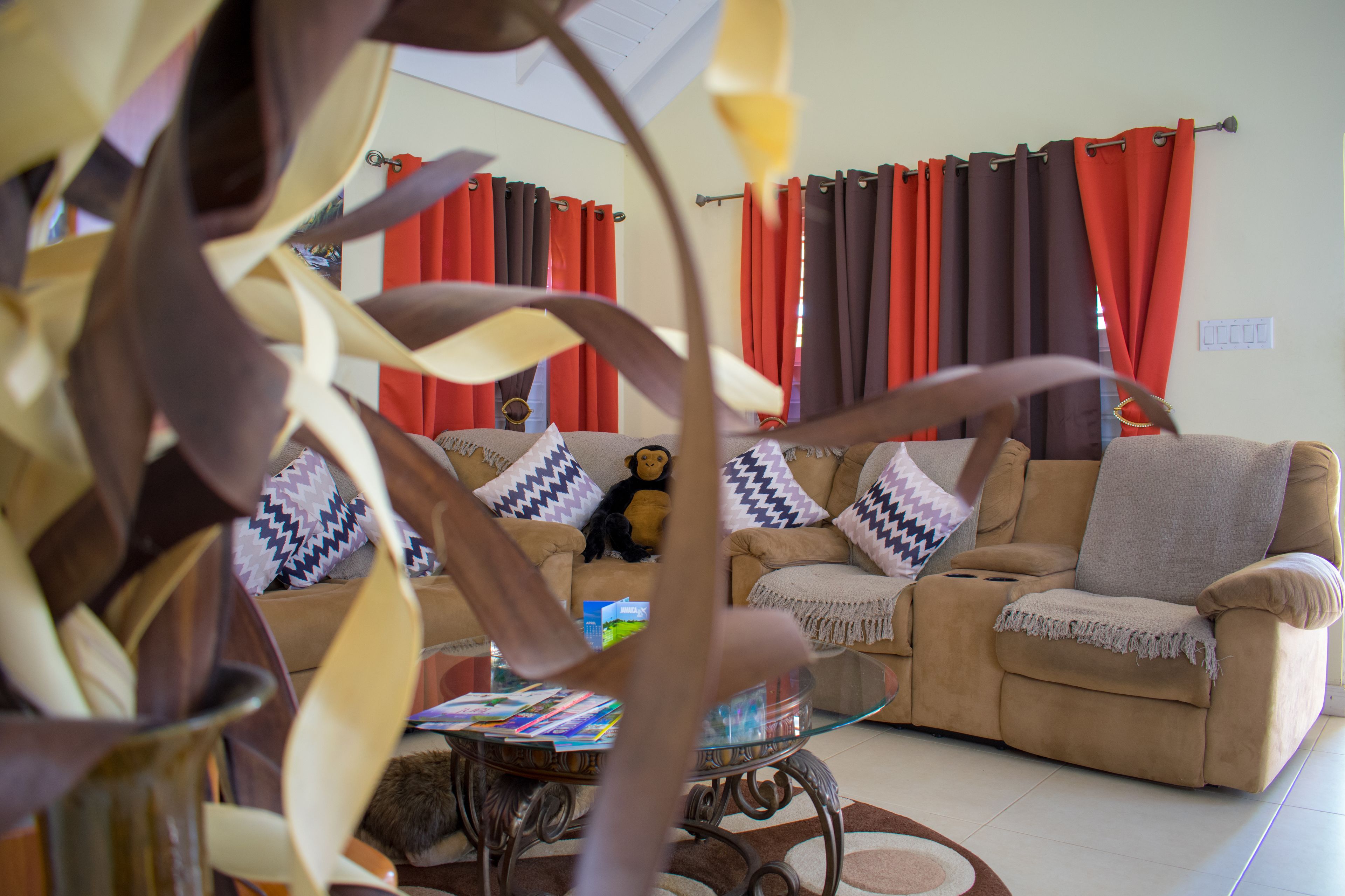 A living room with a beige sofa, a glass coffee table, and red curtains.