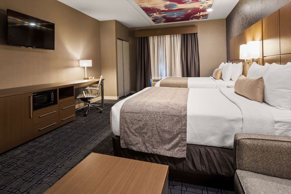 A hotel room with a TV, desk, chair, two beds, and a ceiling mural.