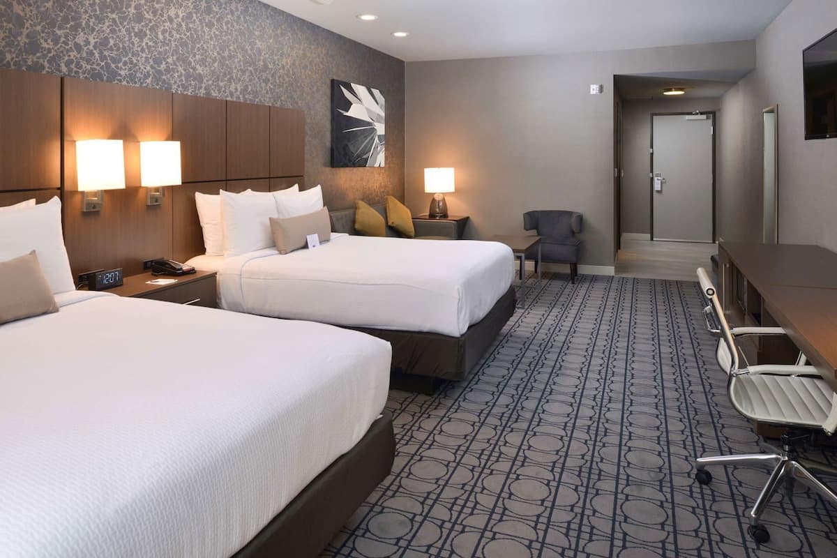 A hotel room with two beds, a desk, a chair, and a bathroom door.