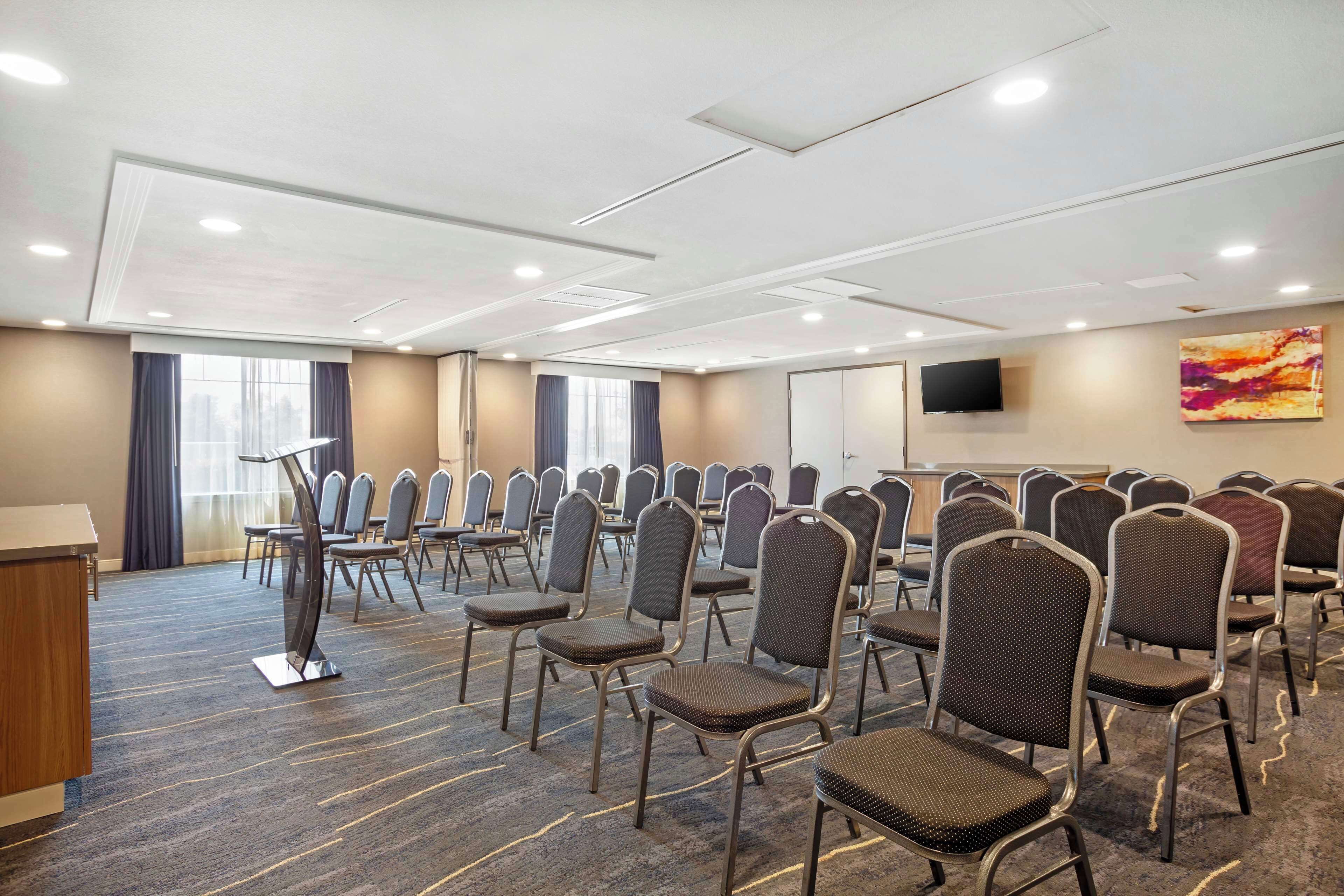 Un salón de conferencias con filas de sillas, un atril y una pantalla grande.