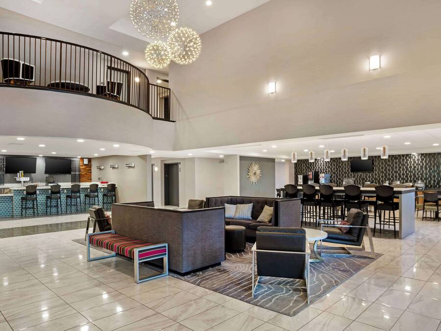 Un lobby espacioso con techo alto, zona de estar central, bar y una escalera que lleva a un nivel superior.