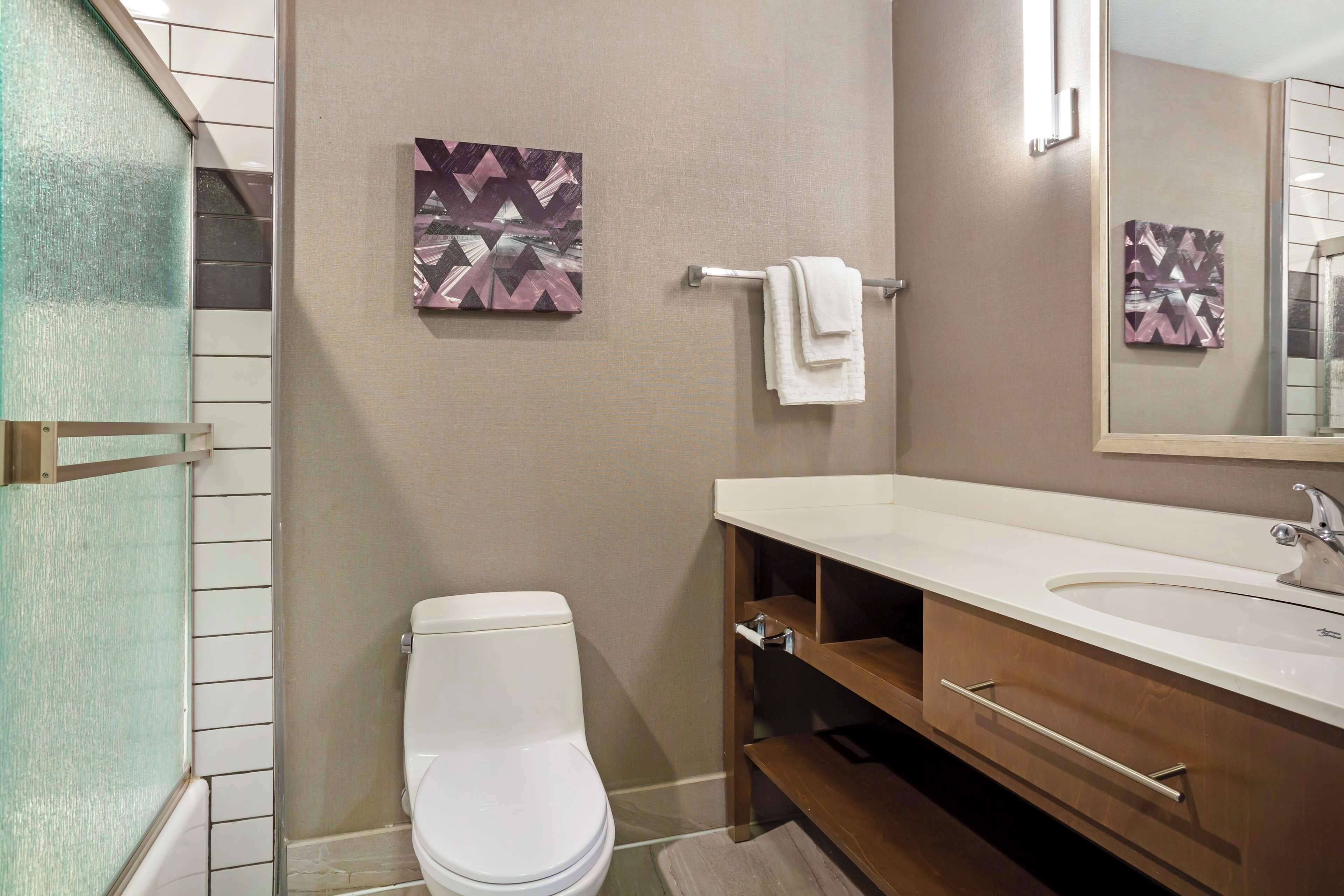 Un baño moderno con un inodoro blanco, un tocador de madera con lavabo y dos obras de arte colgadas en la pared.