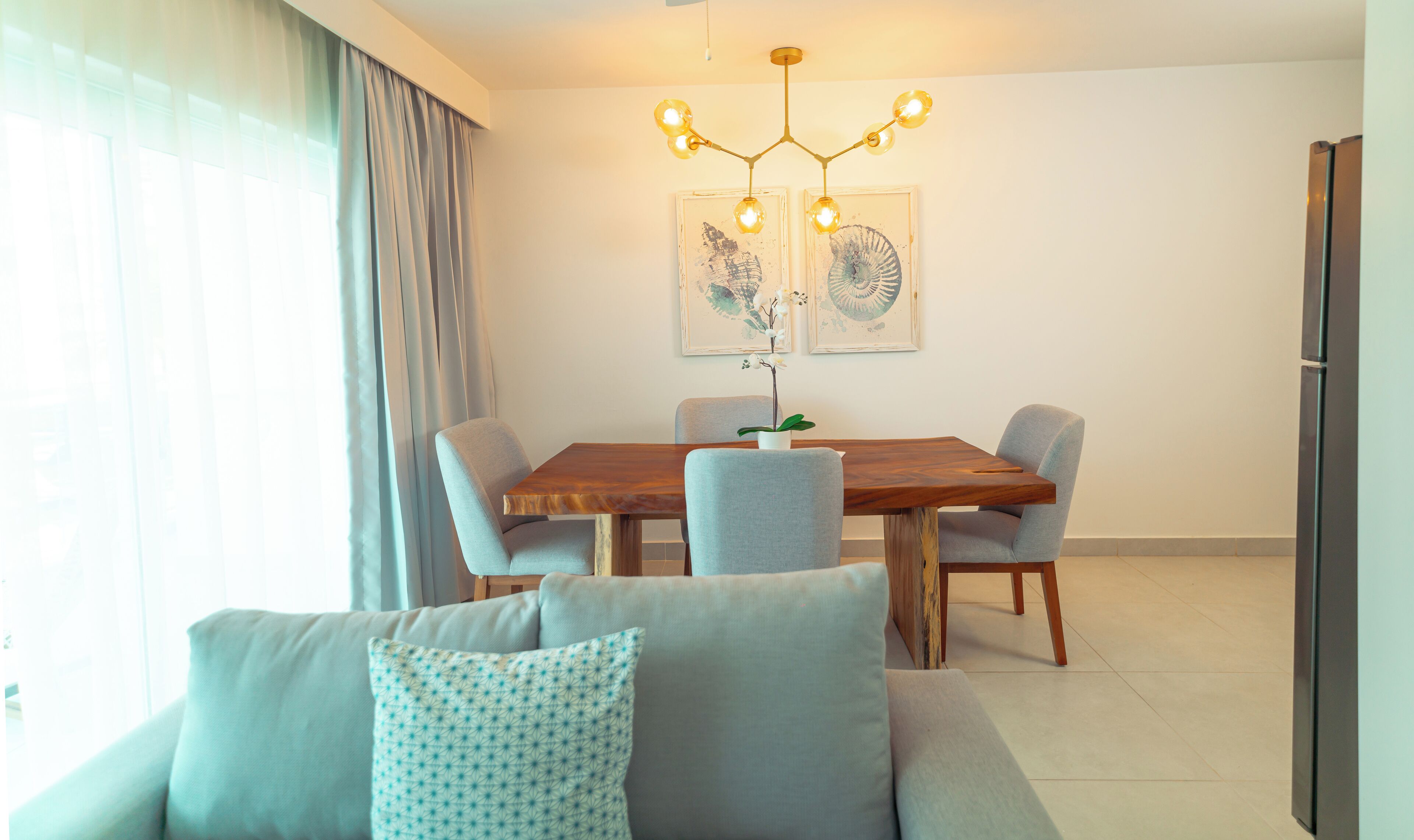 A modern dining area with a wooden table, grey upholstered chairs, and a chandelier.