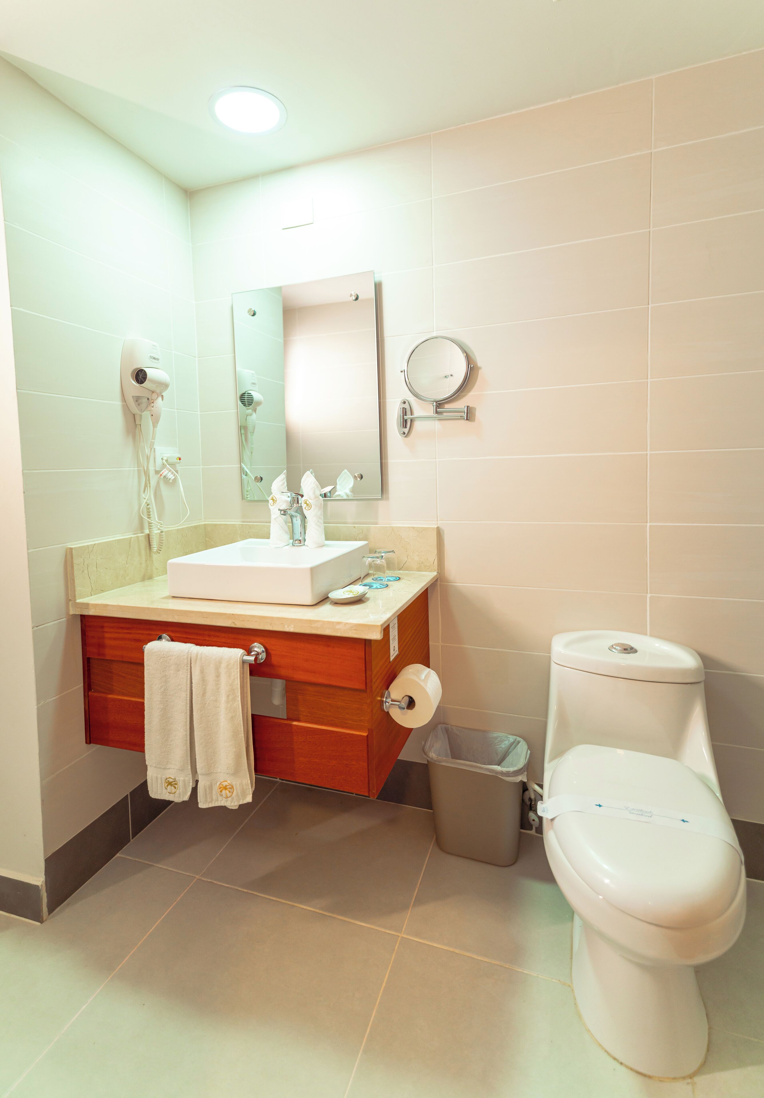 Un baño con lavamanos, espejo, inodoro y un cubo de basura.