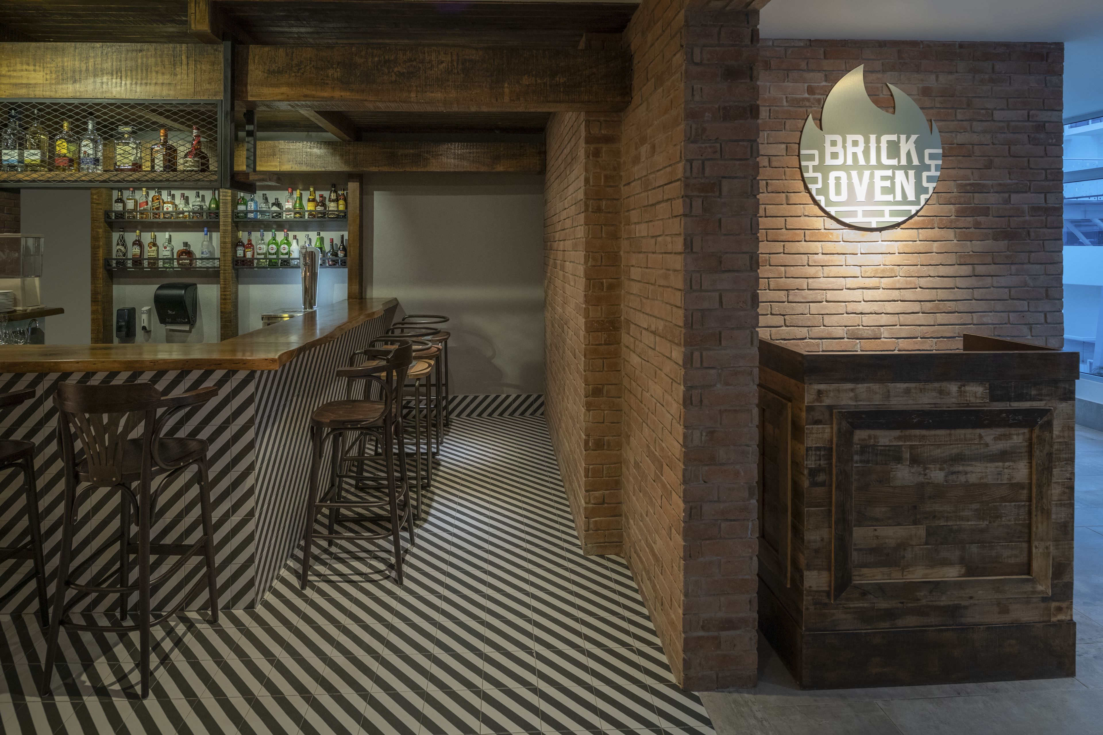 A bar area with a brick wall, a sign reading "BRICK OVEN", and a patterned floor.