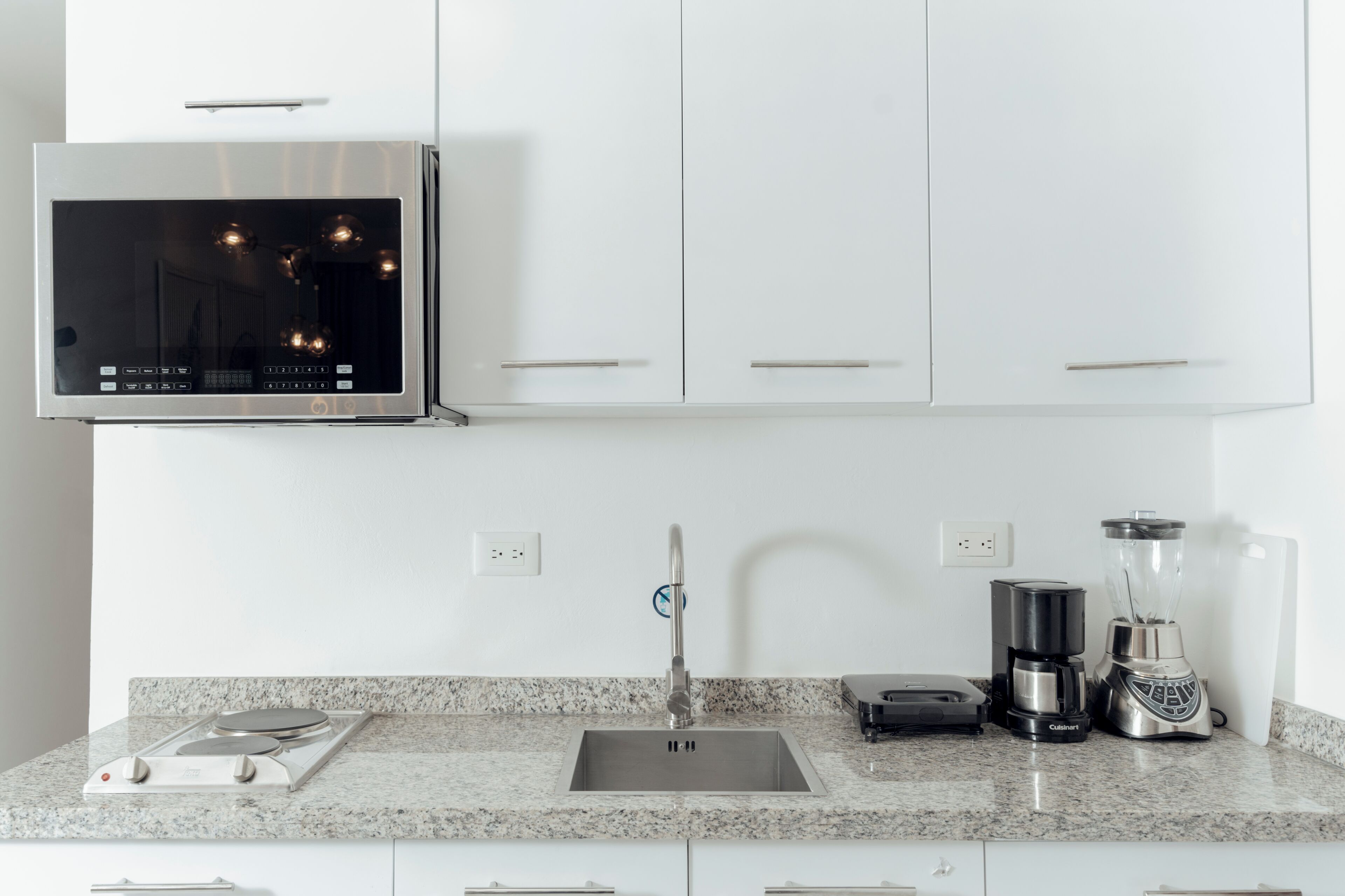 A modern kitchen with a built-in microwave, a coffee maker, a blender, and a granite countertop.