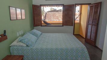 A bedroom with a bed, a window with open shutters, a wall-mounted air conditioner, and a wooden nightstand.
