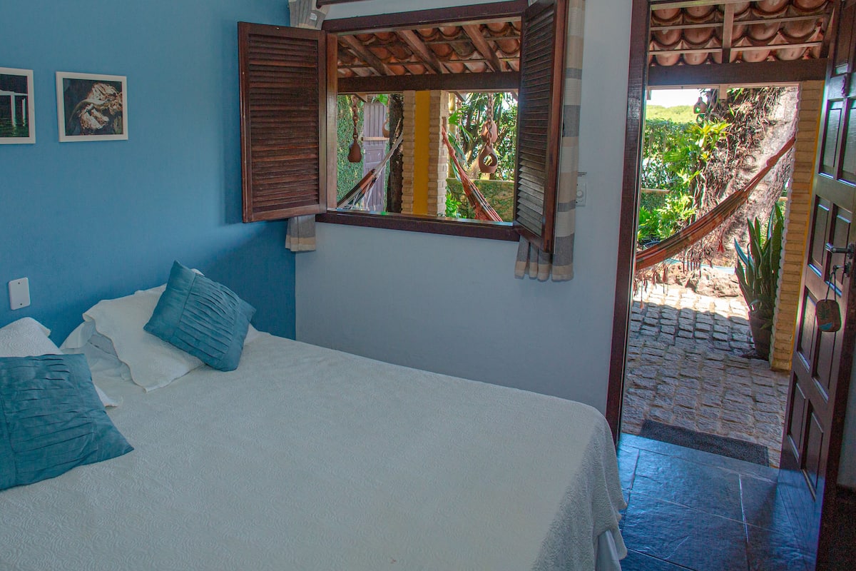 Ein Schlafzimmer mit Bett, Kissen, einem Fenster mit Rollläden und Wandbildern.