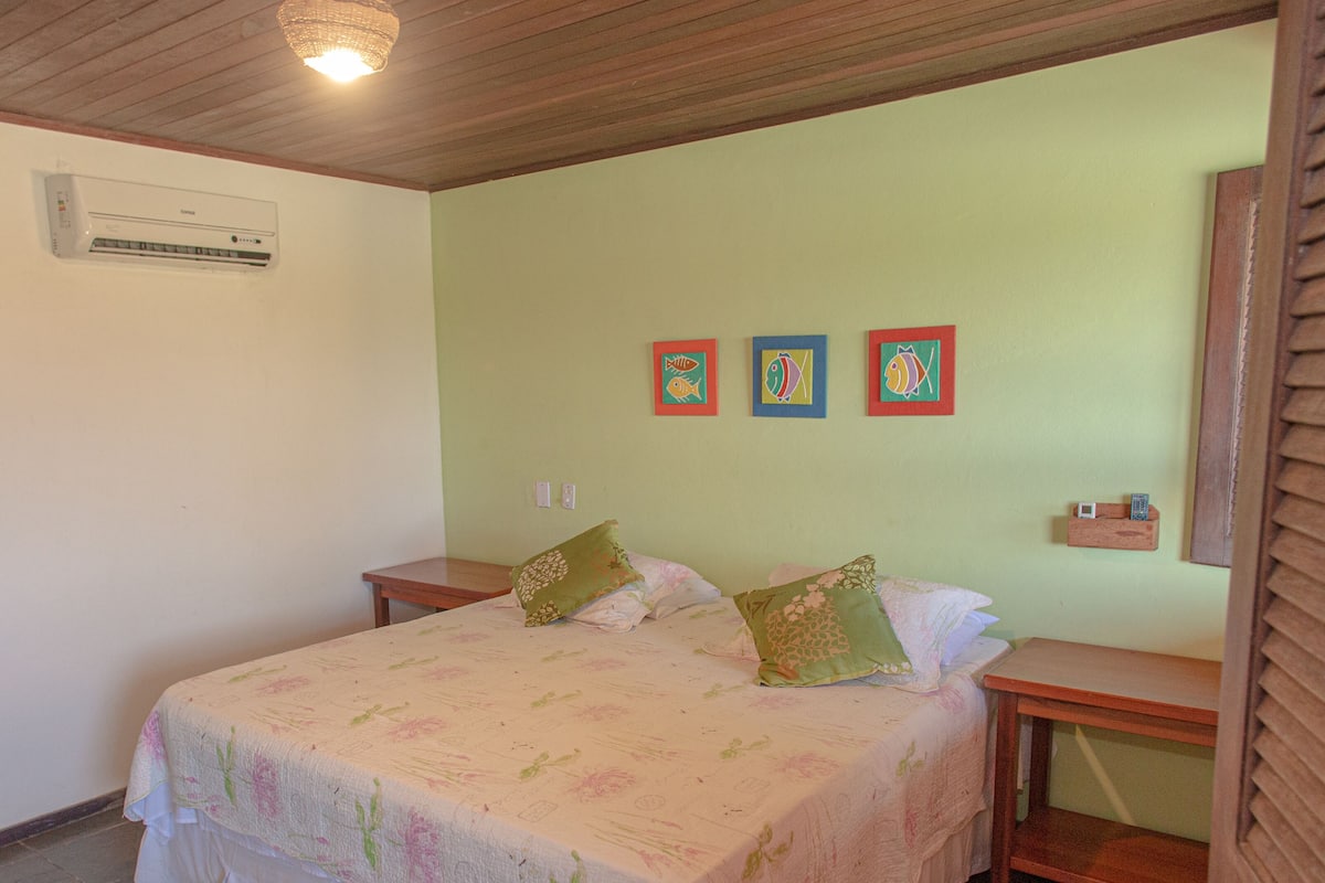 Ein Schlafzimmer mit einem Bett, zwei Nachttischen, einer Wand-Klimaanlage und drei gerahmten Fischbildern.