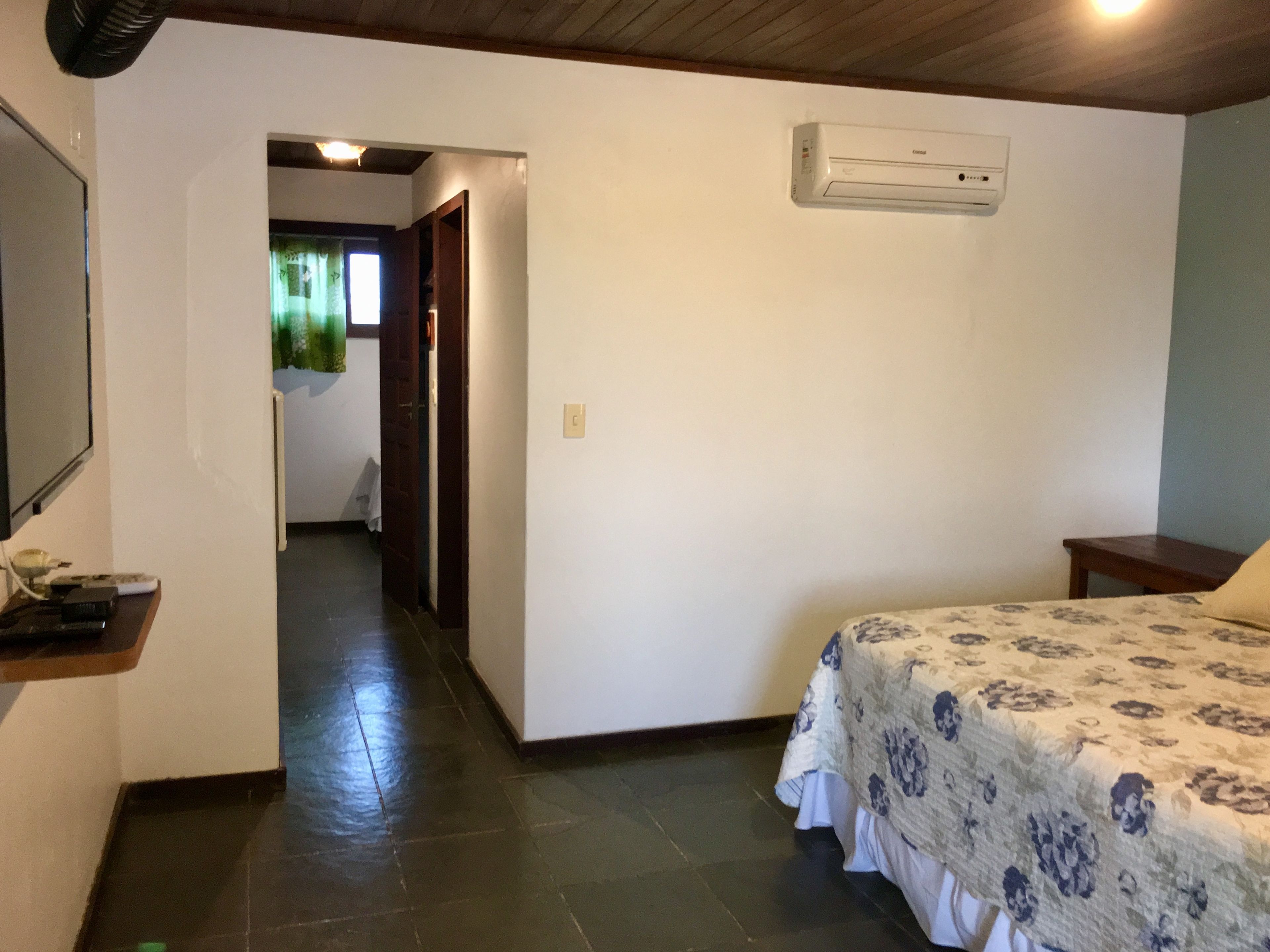 Un dormitorio con una cama, una mesita de noche, un aire acondicionado instalado en la pared y una puerta que da a otra habitación.