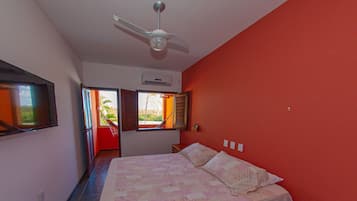 A bedroom with a bed, a ceiling fan, a window with shutters, and a view of greenery outside.