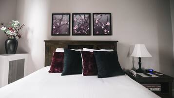 A neatly made bed with three dark pillows, a bedside table with a lamp, a phone, and a book titled "Grand Tour Rome".