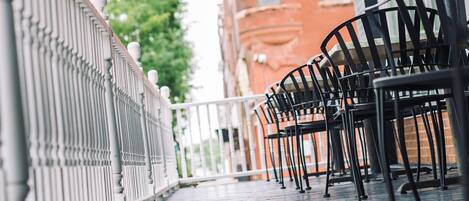 A covered outdoor seating area with metal chairs and a white railing.