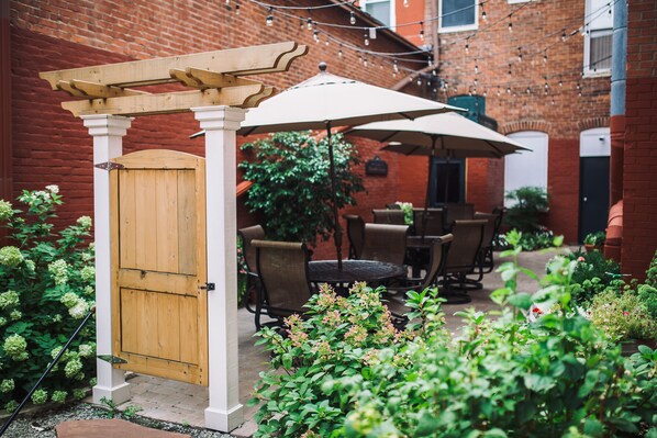 Un espacio de patio con una pérgola de madera, mobiliario exterior y un muro de ladrillo.