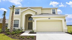 A single-story house with a garage, a front entrance, and a small garden with palm trees. - Providence at Crofton Springs (Davenport)