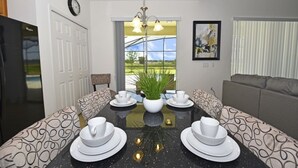 A dining area with a black marble table, white plates, and a potted plant. There is a window with a view of greenery and a sofa in the background. - Providence at Crofton Springs (Davenport)