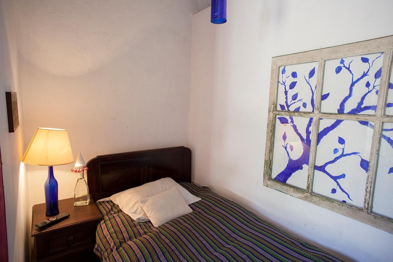 Un dormitorio pequeño con una cama individual, una mesita de noche con lámpara y una ventana empotrada con diseño de árbol.