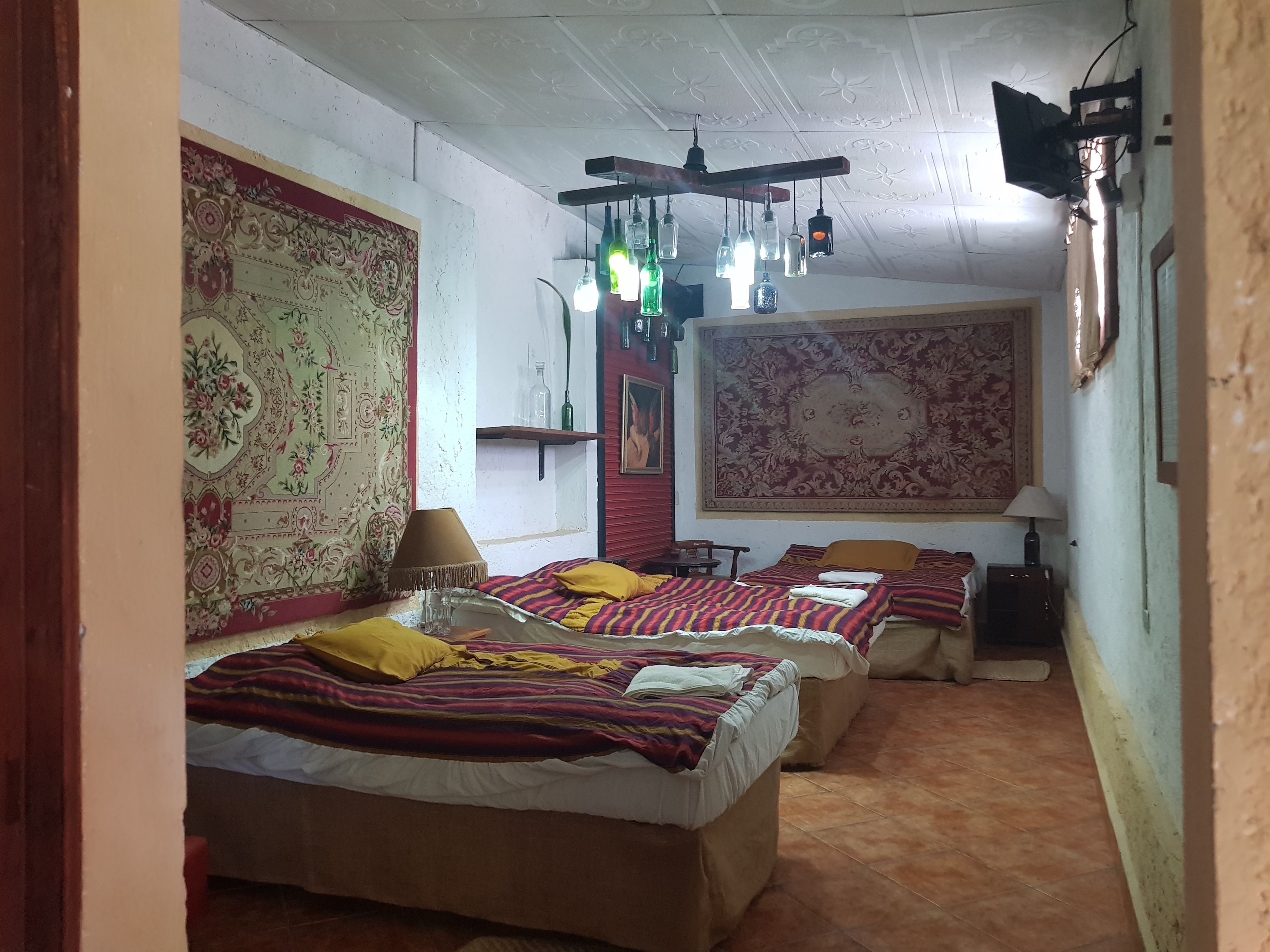 A room with two beds, a large tapestry, and hanging light fixtures.