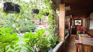 A covered patio area with a brick wall, a wooden ceiling, and a dining table set with a vase of flowers. - Hotel Casa Chapultepec - Hostel (Cobán)