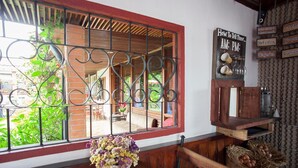 A cozy room with a large window, a wooden bench, a vase of flowers, and a shelf with jars and a sign. - Hotel Casa Chapultepec - Hostel (Cobán)