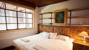A neatly made bed with white linens and towels, a wooden headboard, a painting on the wall, and a window with blinds. - Hotel Casa Chapultepec - Hostel (Cobán)
