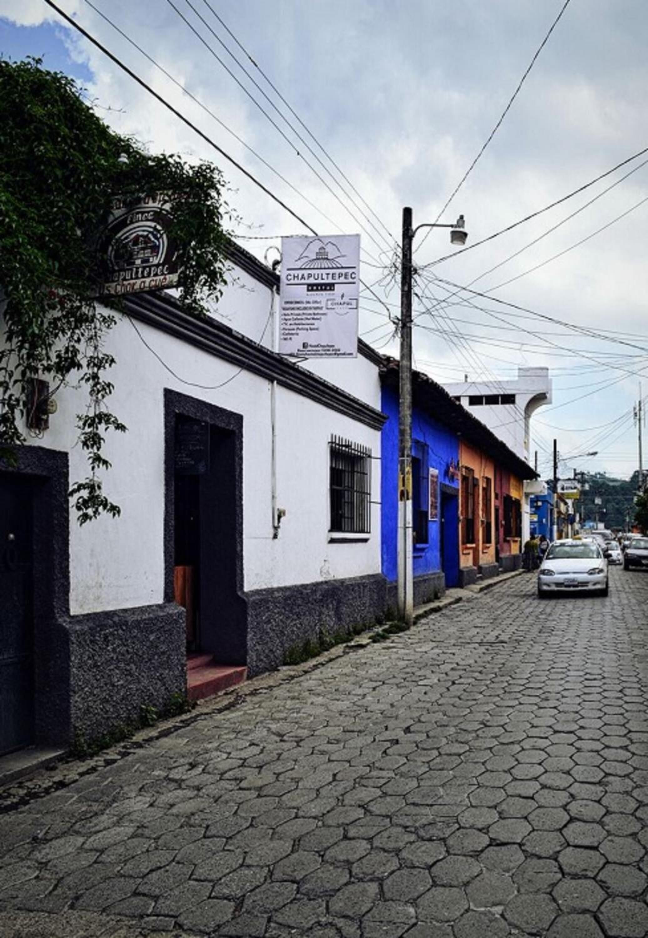 Calle con edificios, incluyendo un edificio blanco con puerta azul y un letrero que dice 'Chapultepec'.