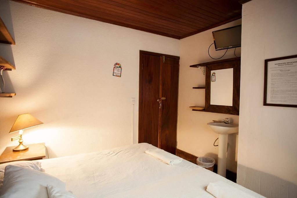 Une chambre d’hôtel avec un lit, une lampe de chevet, une porte en bois, un lavabo et un téléviseur fixé au mur.