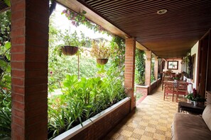 A covered patio with brick columns, hanging planters, and a tiled floor. - Hotel Casa Chapultepec - Hostel (Cobán)
